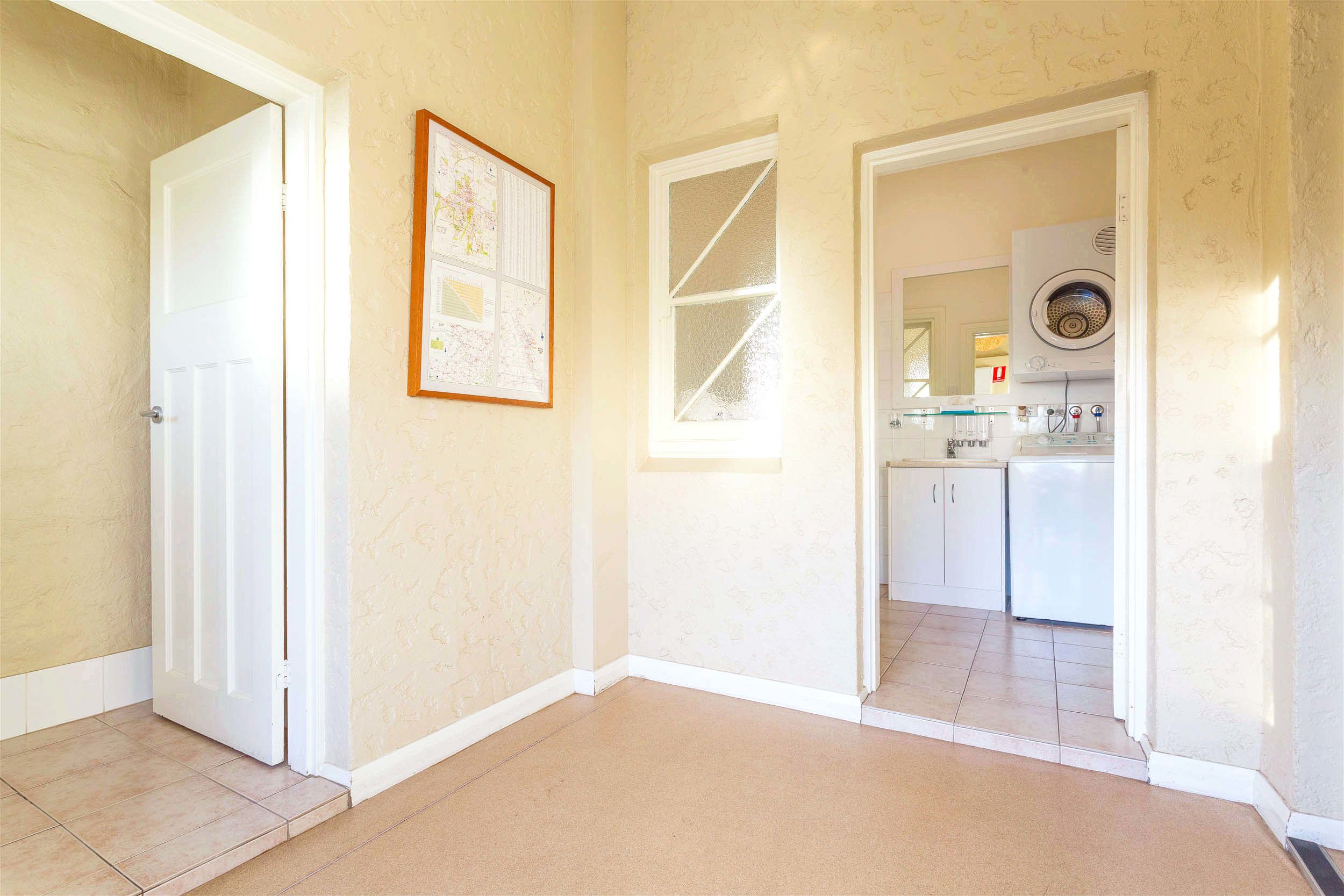 A hallway with a door, a framed map, and a kitchen area with appliances.