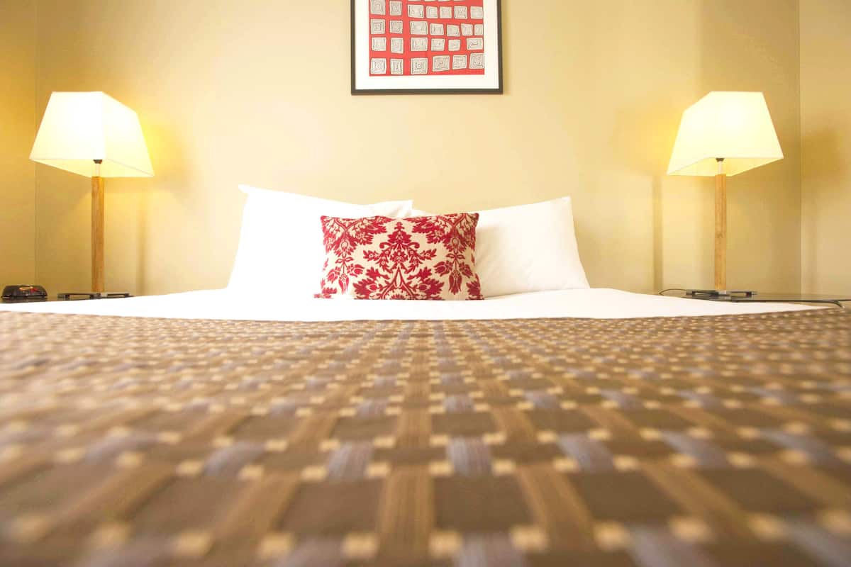 A hotel room with a neatly made bed, two bedside lamps, and a framed picture on the wall.