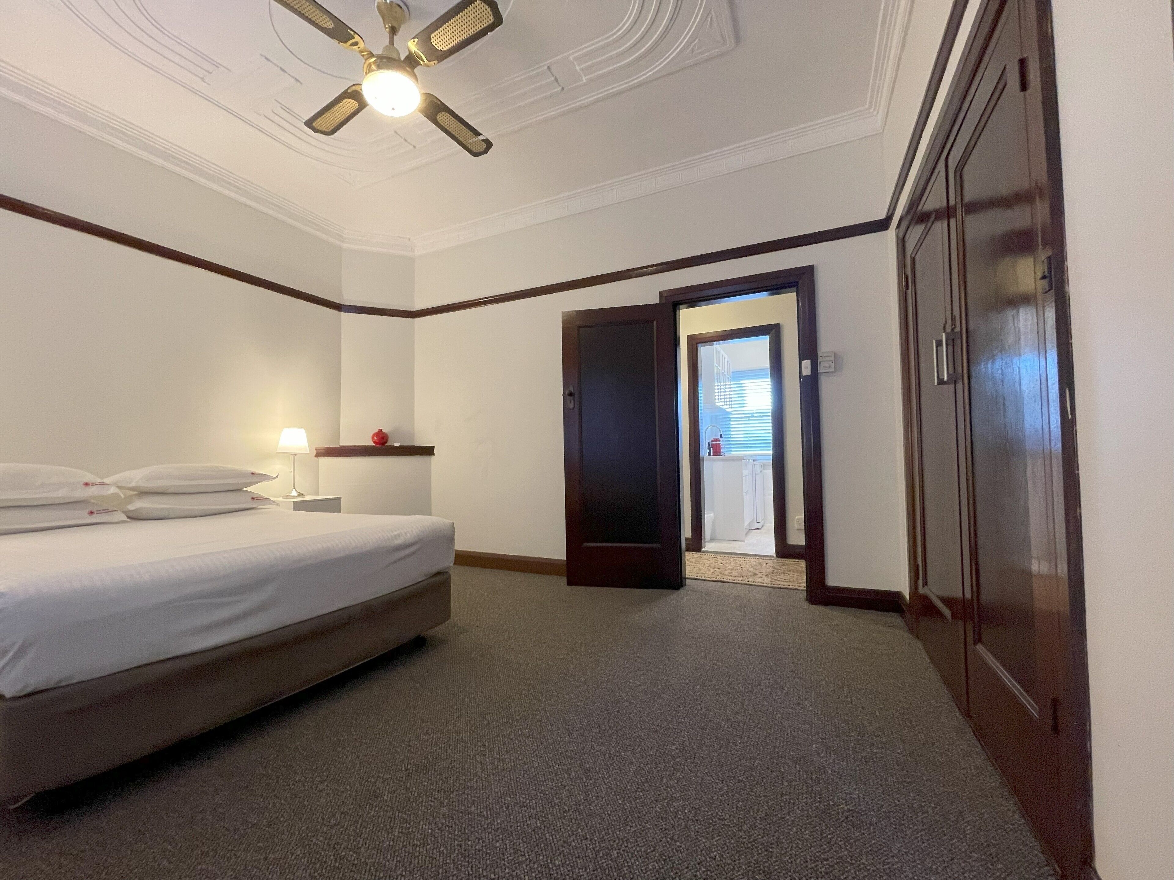 A hotel room with a bed, a nightstand, a lamp, a ceiling fan, and a door leading to a bathroom.
