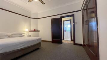 A hotel room with a bed, a nightstand, a lamp, a ceiling fan, and a door leading to a bathroom.