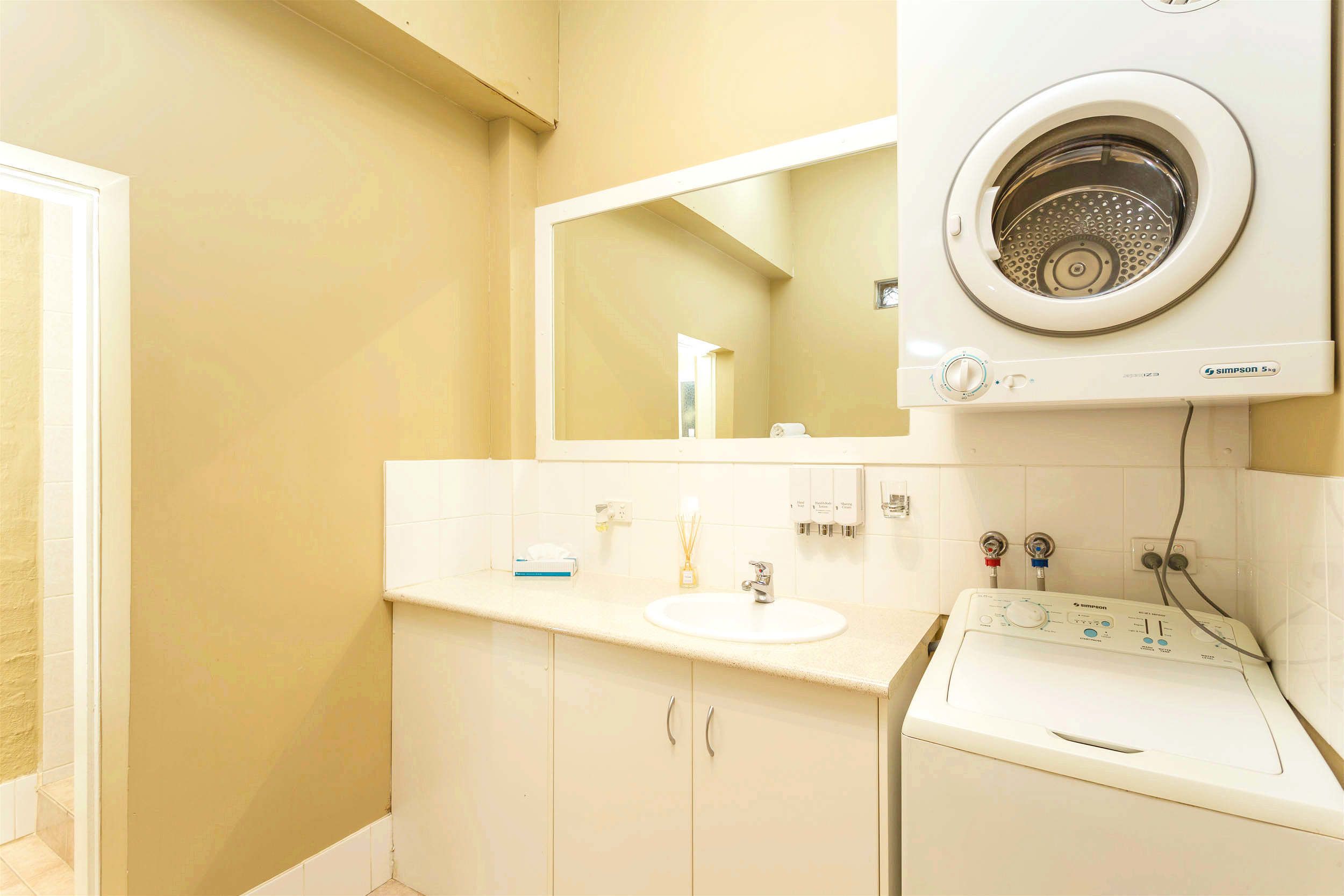 Un baño con lavamanos blanco, espejo y lavadora integrada.