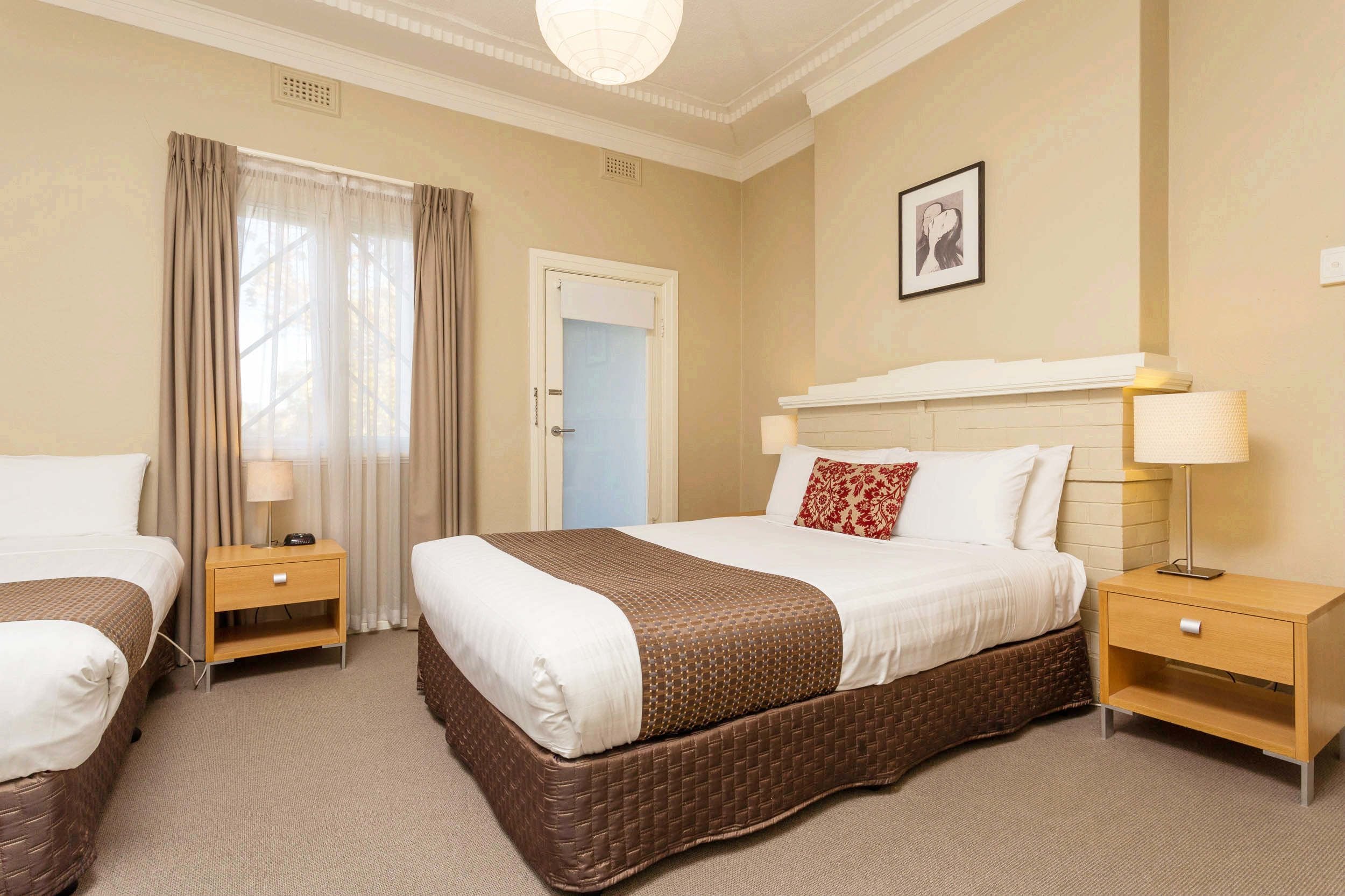 A hotel room with two beds, a large window with curtains, a fireplace, and a framed picture on the wall.