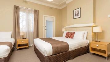 A hotel room with two beds, a large window with curtains, a fireplace, and a framed picture on the wall.