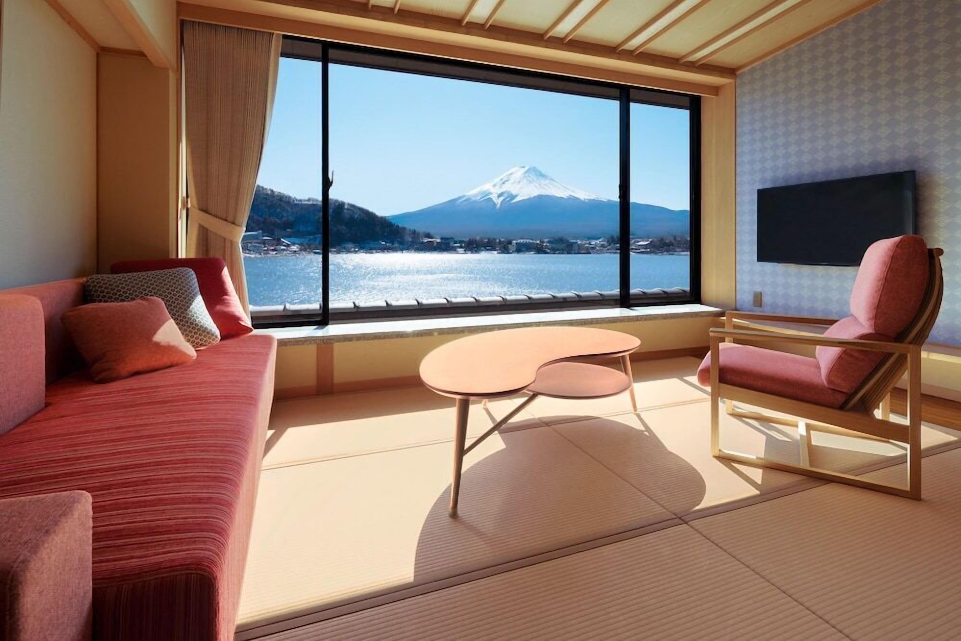 Una habitación con sofá, una silla, una mesita, televisor y un ventanal con vistas a la montaña.