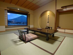 A traditional Japanese room with tatami flooring, a low table, and a view of a mountain.