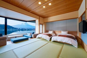 A hotel room with a large bed, a TV, tatami mats, and a view of a mountain.