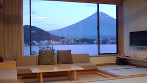 A living room with a sofa, a coffee table, tatami mats, a TV, and a view of a mountain and lake. - Ubuya (Fujikawaguchiko)