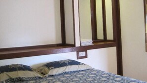 Un dormitorio con una cama, dos almohadas, un cabecero de madera y una pequeña repisa con una toalla doblada.