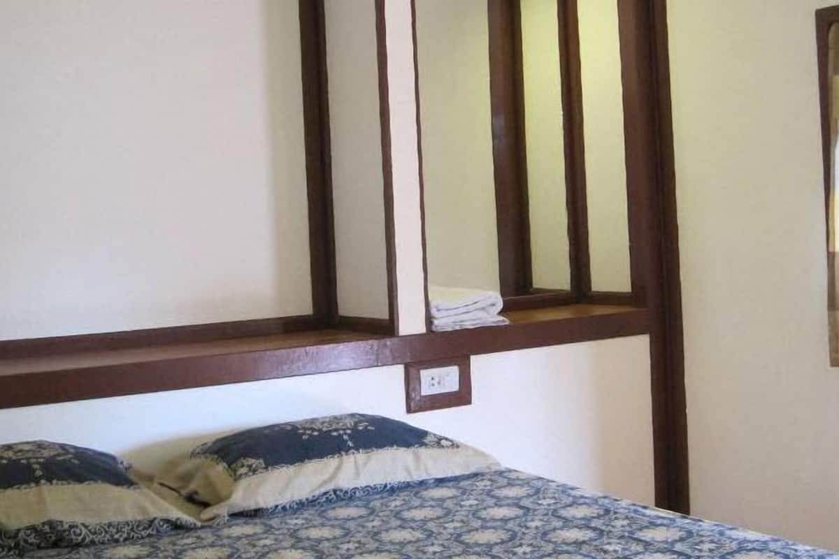 Un dormitorio con una cama, dos almohadas, un cabecero de madera y una pequeña repisa con una toalla doblada.