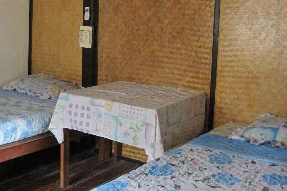 Dos camas individuales con cabeceros y patas de madera, una mesita con un mapa, y un interruptor de luz en la pared.