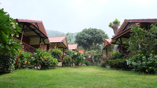 A row of traditional-style cottages with red roofs and wooden structures, surrounded by lush greenery and a grassy lawn.