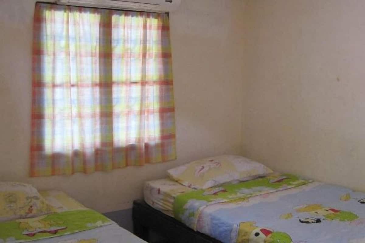 Una habitación pequeña y sencilla con dos camas individuales, una ventana con cortinas coloridas y una pared lisa.