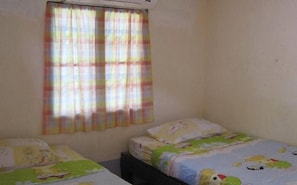 A small, simple room with two single beds, a window with colorful curtains, and a plain wall.