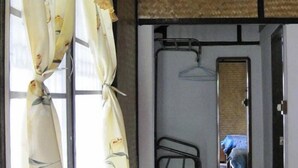 Una habitación con cama, perchero y ventana con cortinas.