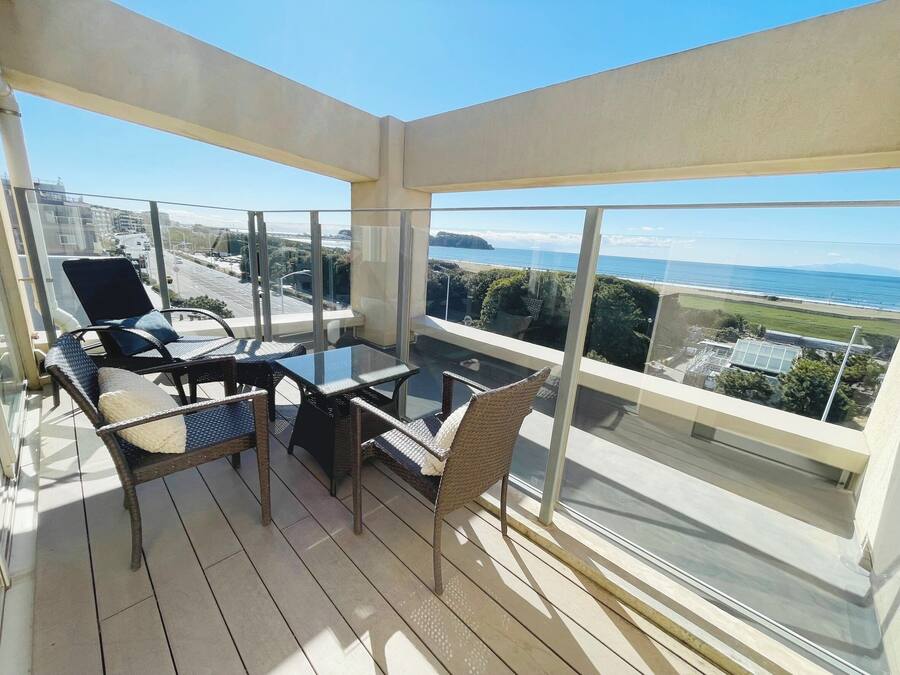 A balcony with a glass table and chairs, overlooking a coastal view.
