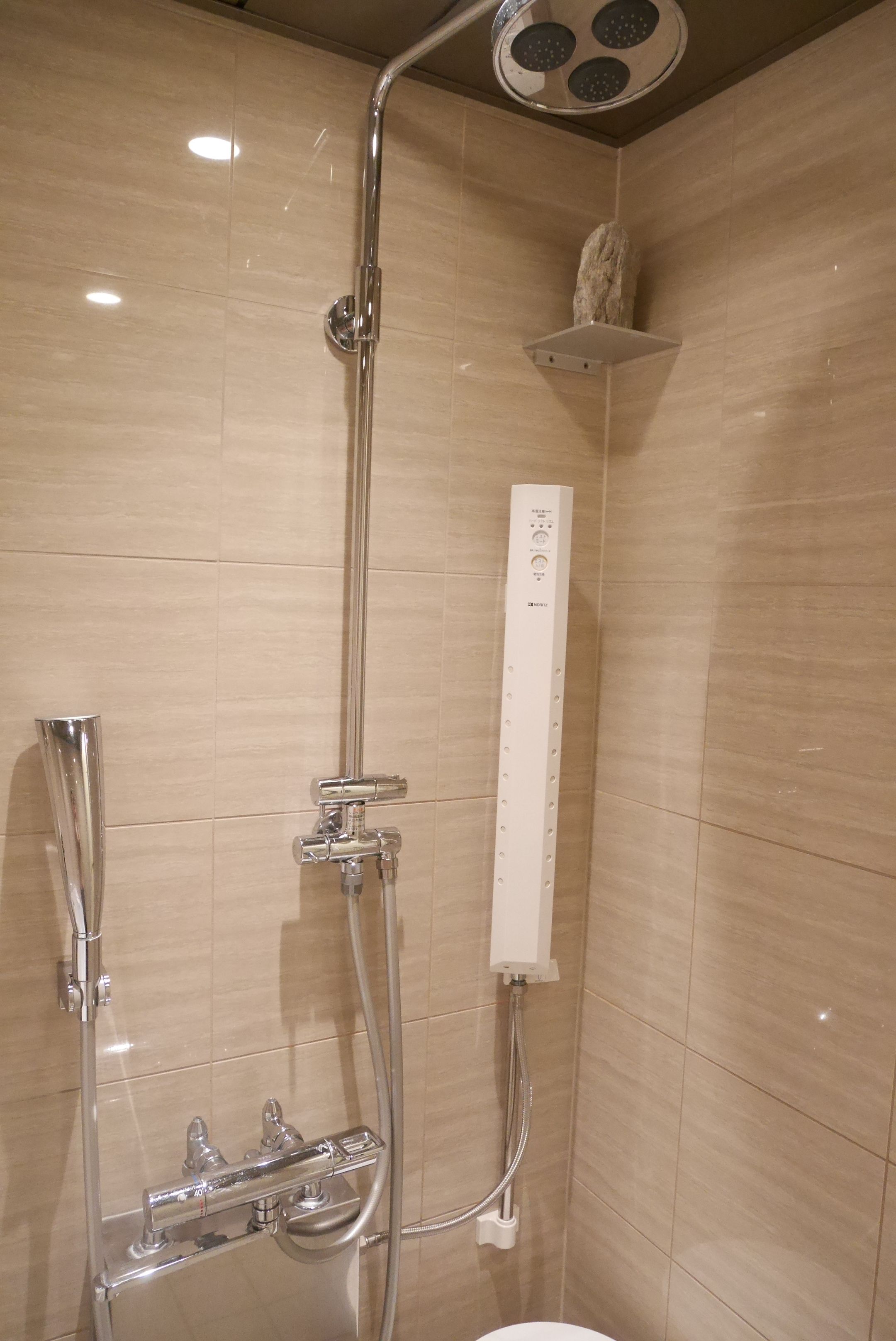 A modern shower with a control panel, a handheld showerhead, and a handheld faucet.