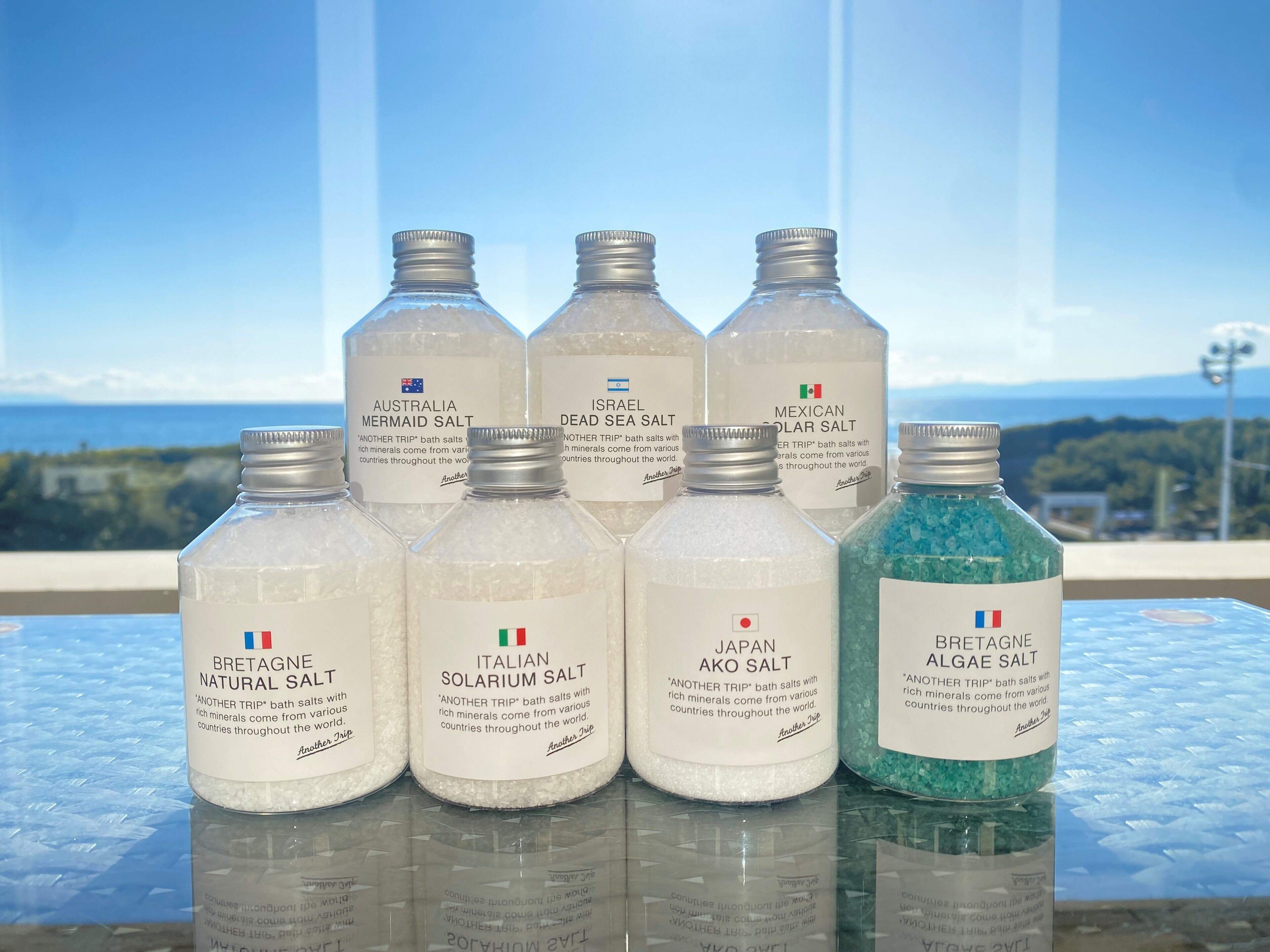 A collection of bath salts on a glass table with a scenic view in the background.