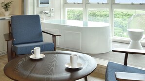A modern bathroom with a bathtub, a sink, and a large window offering a view of greenery and the sea. - Breath Hotel (Fujisawa)