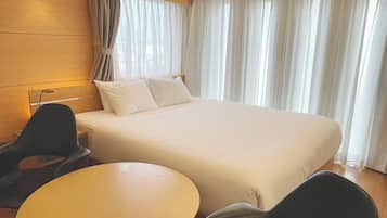 A hotel room with a large bed, two chairs, a small table, and a lamp.