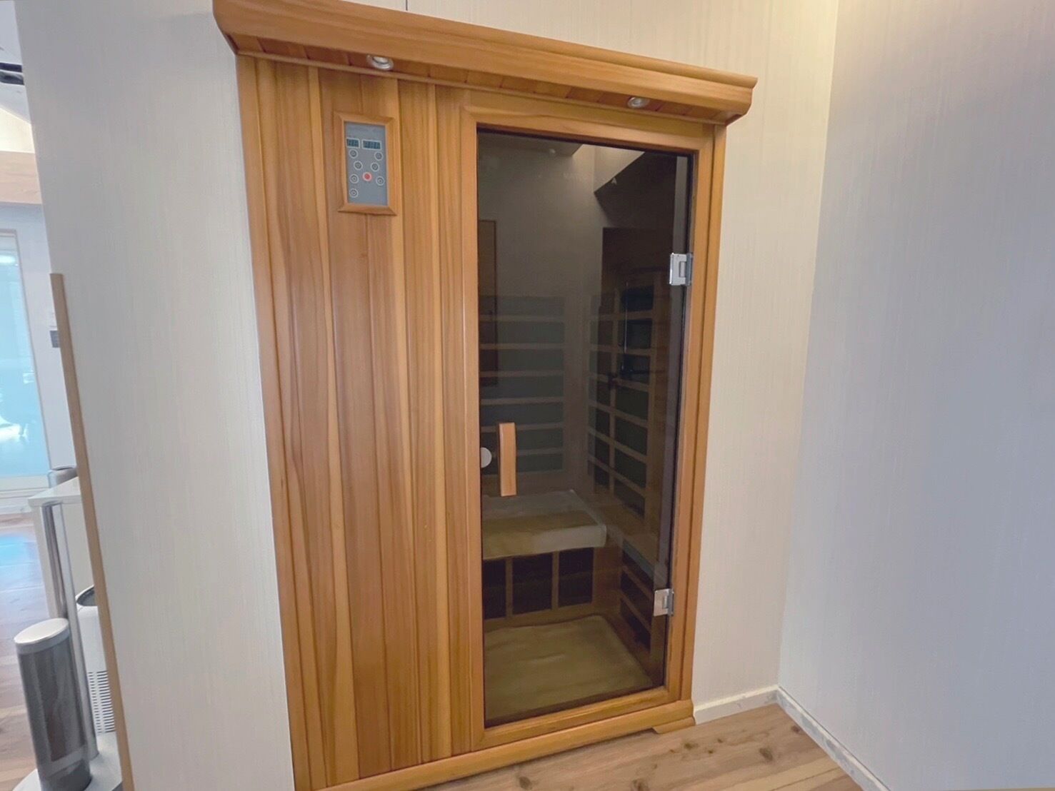 Ein Holzkleiderkasten mit Glastür, einer Bedienkonsole und einem Metall-Mülleimer.