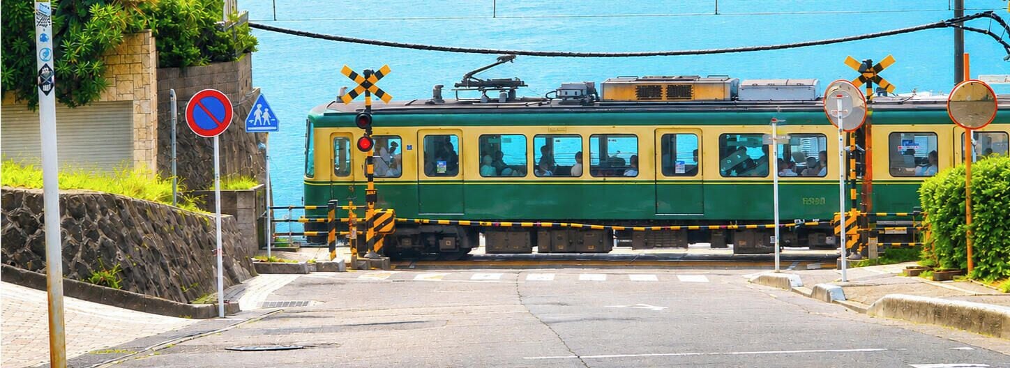 A tram at a railway crossing with a pedestrian crossing sign, a no parking sign, and a no entry sign.