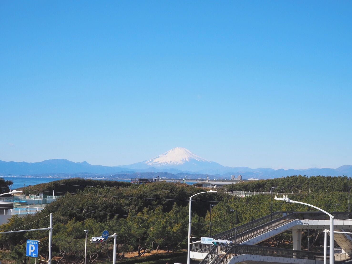 A view of Mount Fuji in the background with a parking sign and a pedestrian bridge in the foreground.