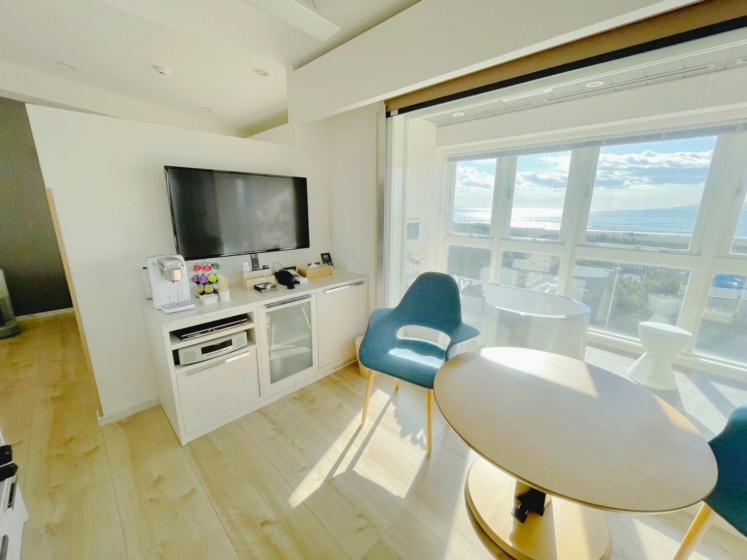A modern room with a flat-screen TV, a small kitchen area, a dining table, and a large window with a view.