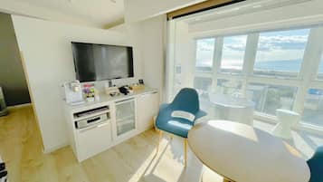 A modern room with a flat-screen TV, a small kitchen area, a dining table, and a large window with a view.