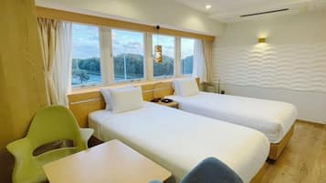 A hotel room with two beds, a desk, a chair, and a window with a view of trees.