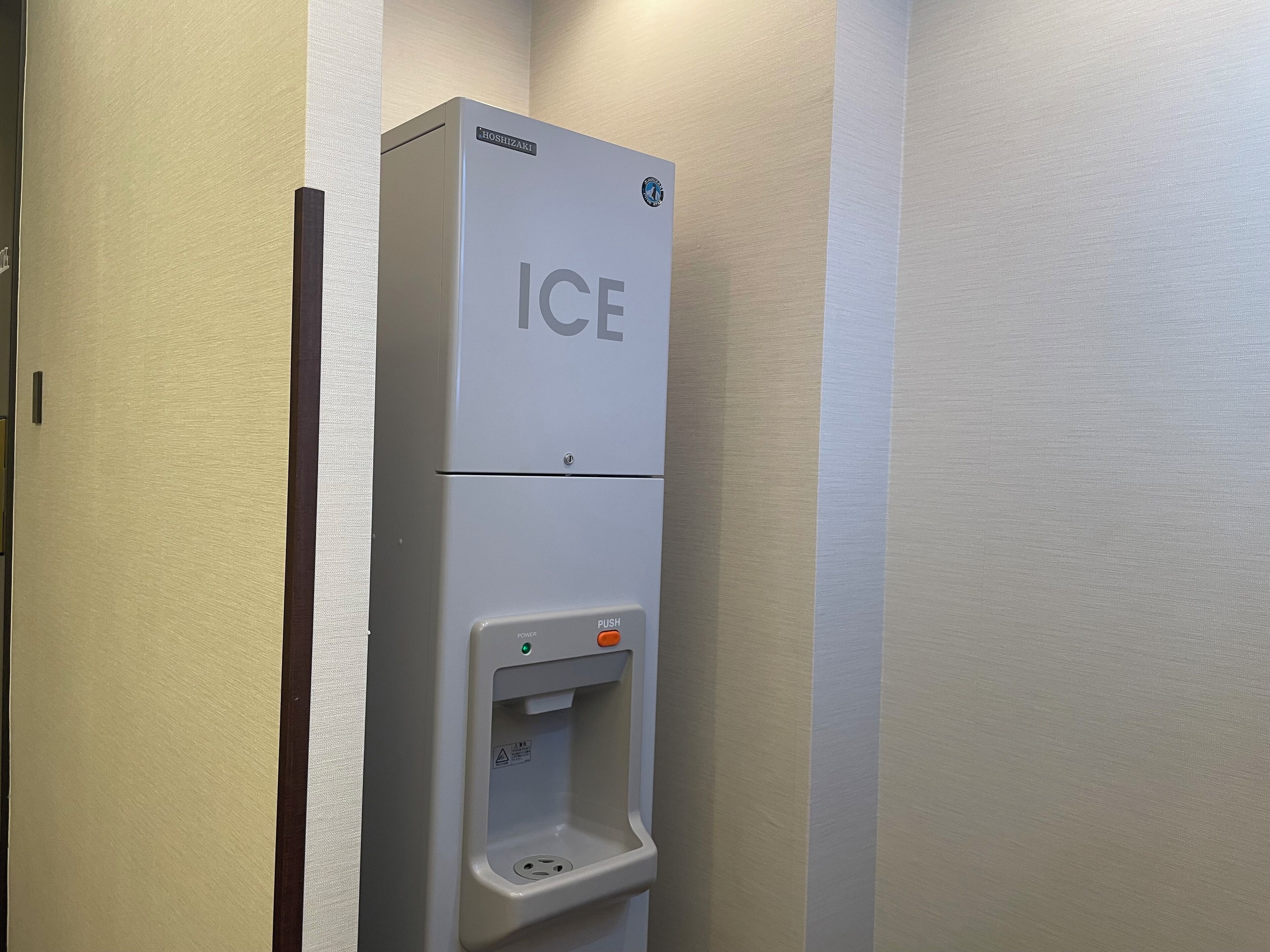 Ein an der Wand befestigter Eiswürfelspender mit Druckknopf und Warnhinweis.