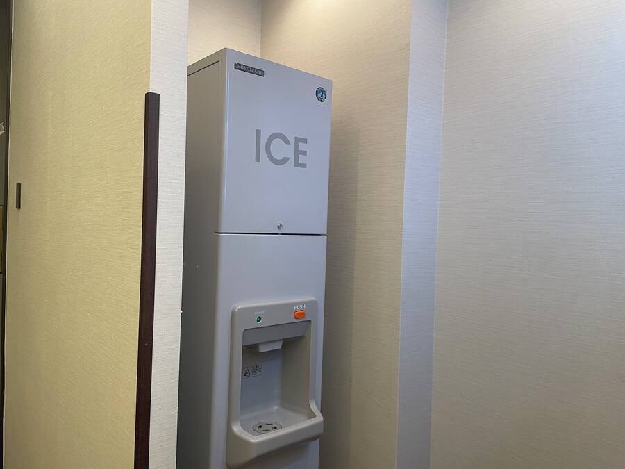 Ein an der Wand befestigter Eiswürfelspender mit Druckknopf und Warnhinweis.