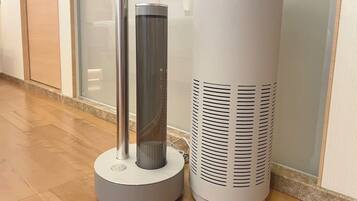 A modern air purifier and a cylindrical device with the brand name 'cado' on a tiled floor.