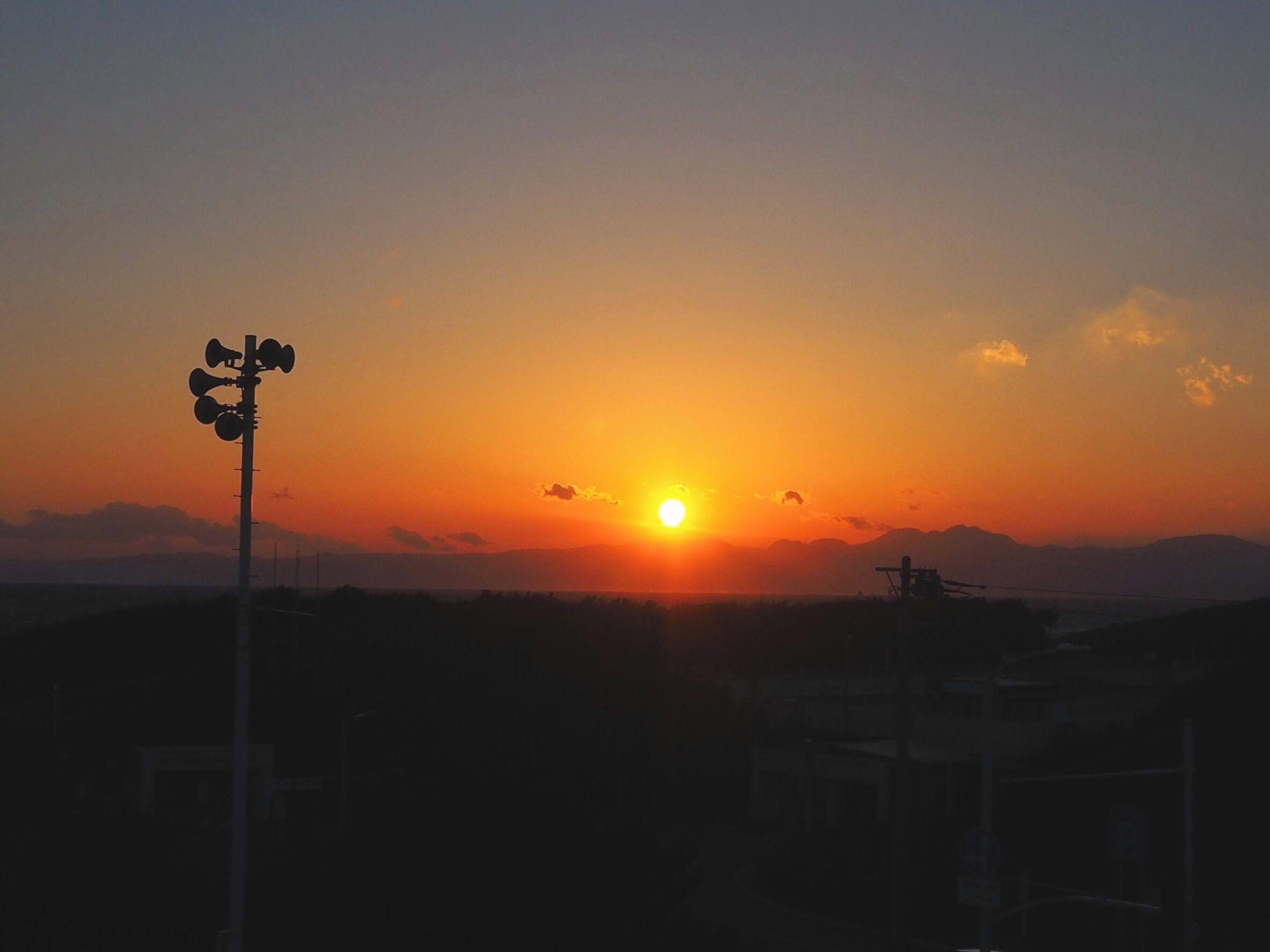 A sunset with a silhouette of a communication tower and distant mountains.