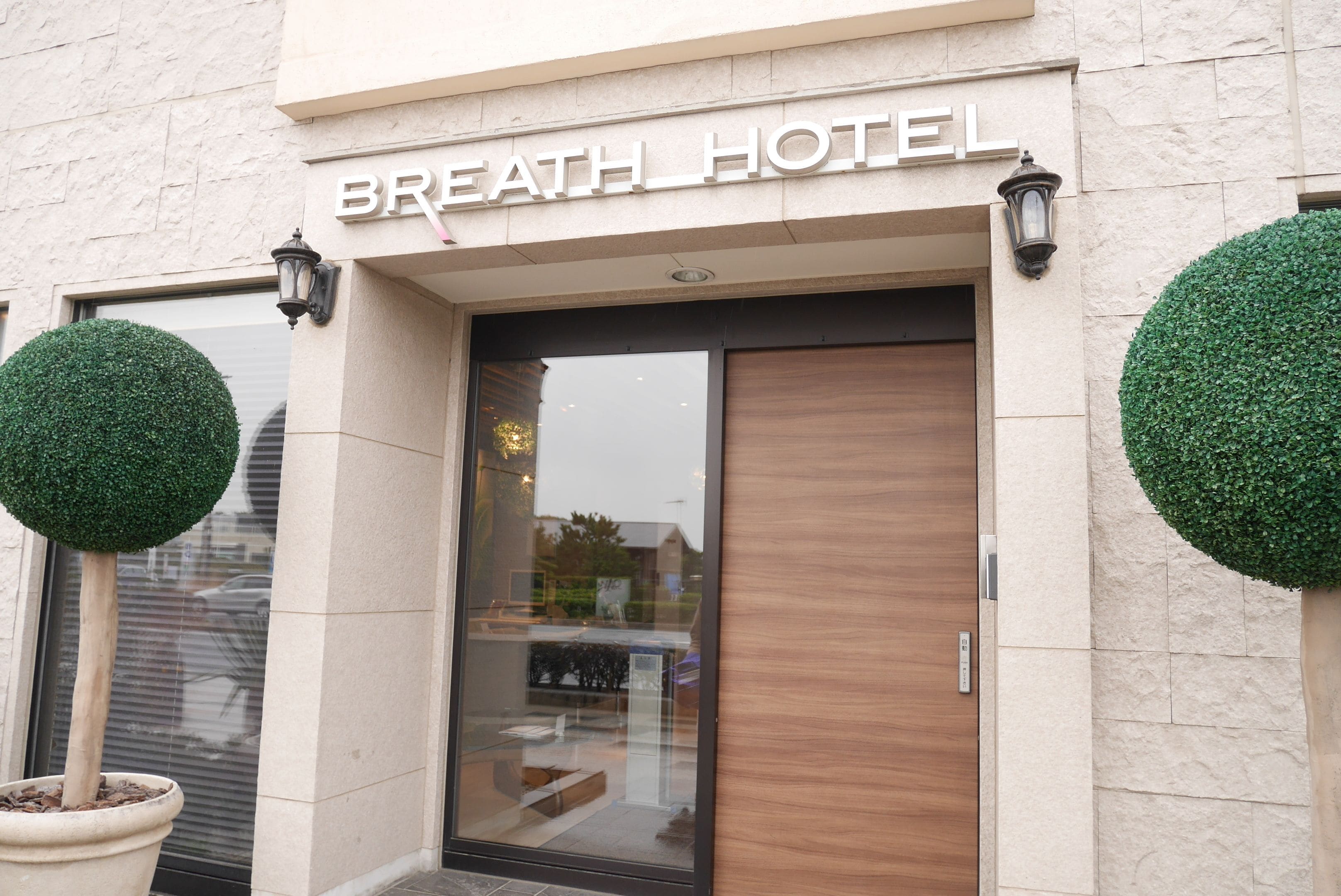 Exterior del Hotel Breath, con fachada moderna, puertas de vidrio grandes y dos macetas redondas.