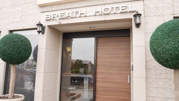 Exterior del Hotel Breath, con fachada moderna, puertas de vidrio grandes y dos macetas redondas.
