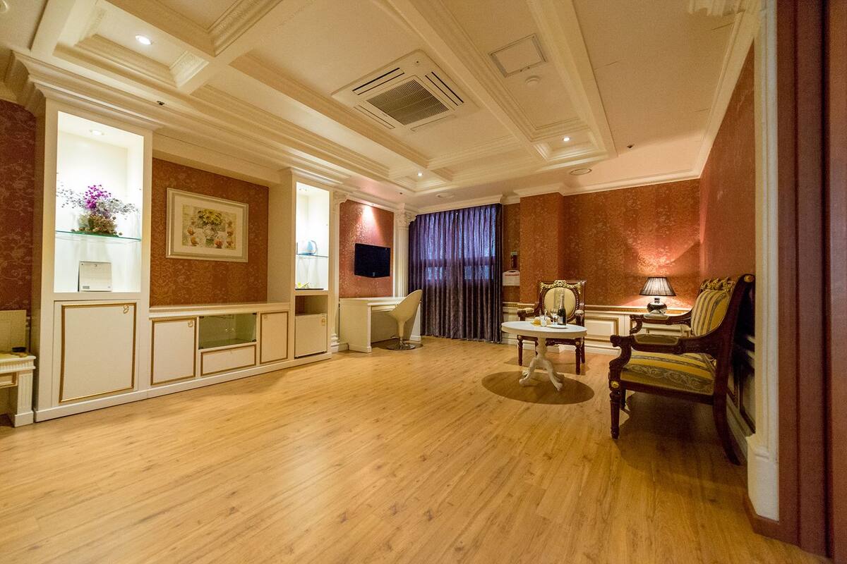 A spacious room with a wooden floor, a desk with a chair, a television, and a dining area with a table and chairs.