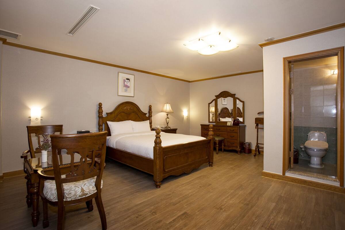A bedroom with a wooden bed, a wooden dresser, a wooden chair, and a wooden table.