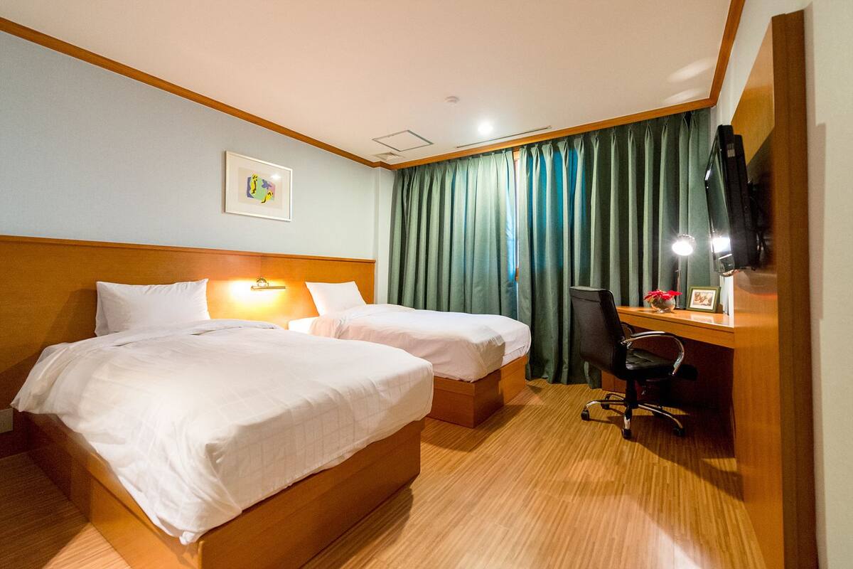 A hotel room with two beds, a desk, a chair, a television, and a picture on the wall.