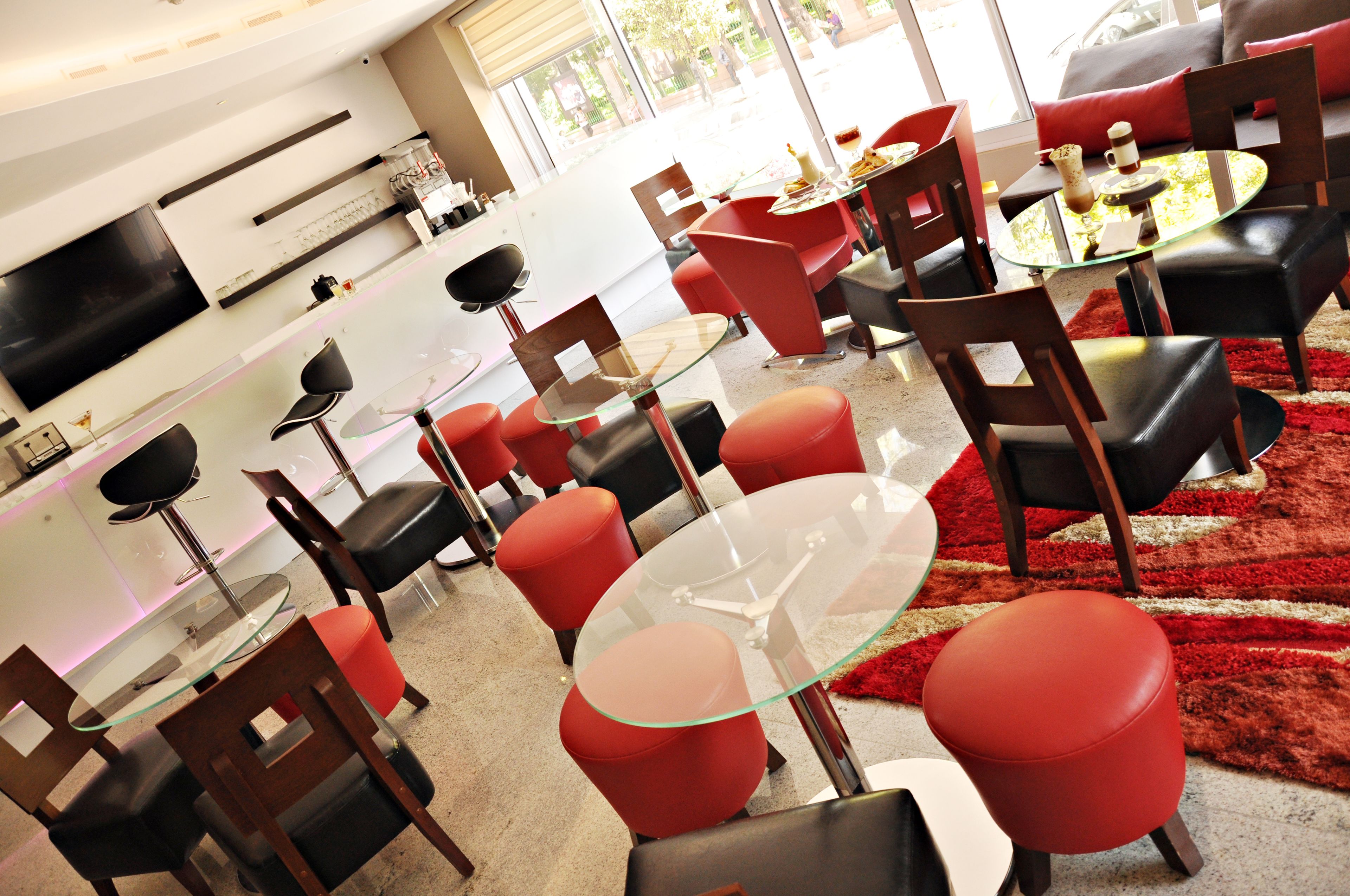 A modern living room with red and black furniture, a glass coffee table, and a flat-screen TV mounted on the wall.