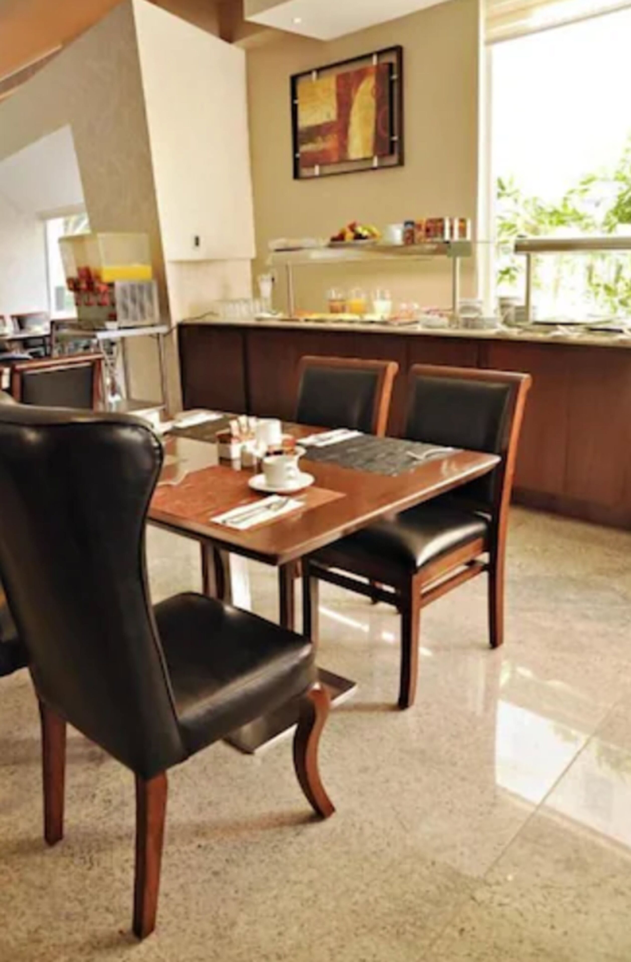 Un comedor con una mesa de madera y sillas negras, una cocina al fondo y un ventanal con vistas a zonas verdes.