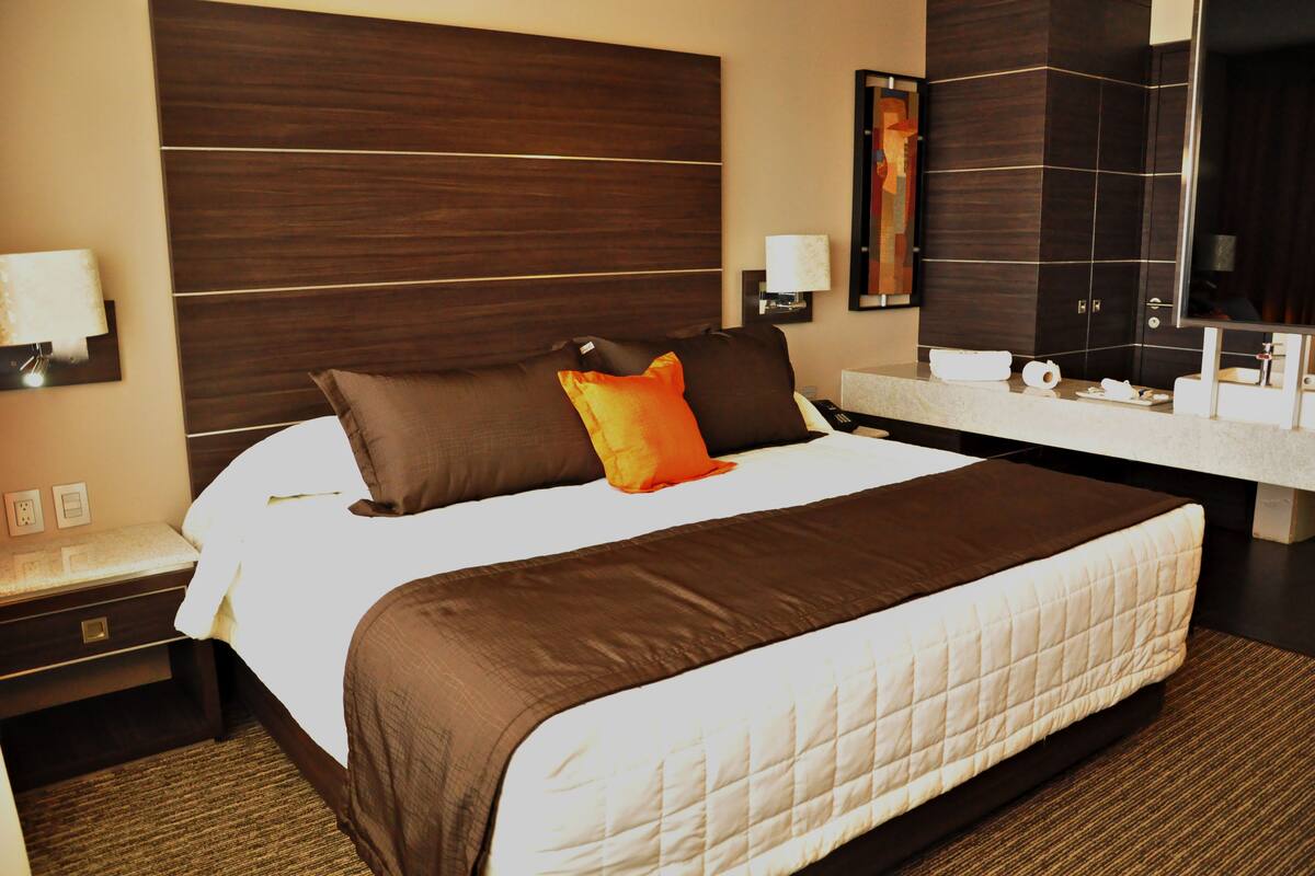A hotel room with a large bed, a bedside table, a nightstand, a bathroom with a mirror, and a towel rack.