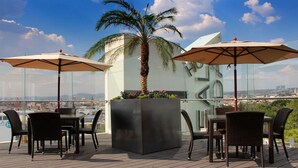 A rooftop terrace with outdoor seating, palm trees, and a city view. - Hotel Real Alameda (Querétaro)