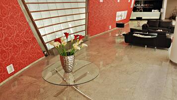 A hotel lobby with a reception desk, a glass table with a vase of flowers, and a seating area with sofas.