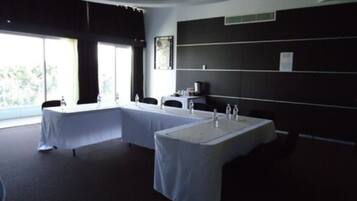 Una habitación de hotel moderna con techo curvo, un ventanal con vistas, una mesa larga con sillas y una pared oscura con estantería.