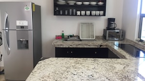 A kitchen with a stainless steel refrigerator, a microwave, a coffee maker, and a shelf with dishes and cups. - La Playa Condo (Playa del Carmen)