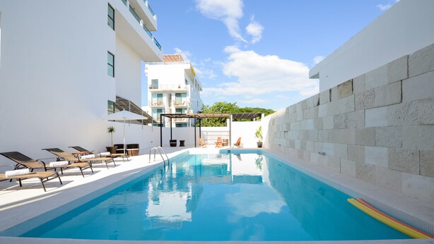 A swimming pool with lounge chairs, a pergola, and a stone wall. - La Playa Condo (Playa del Carmen)