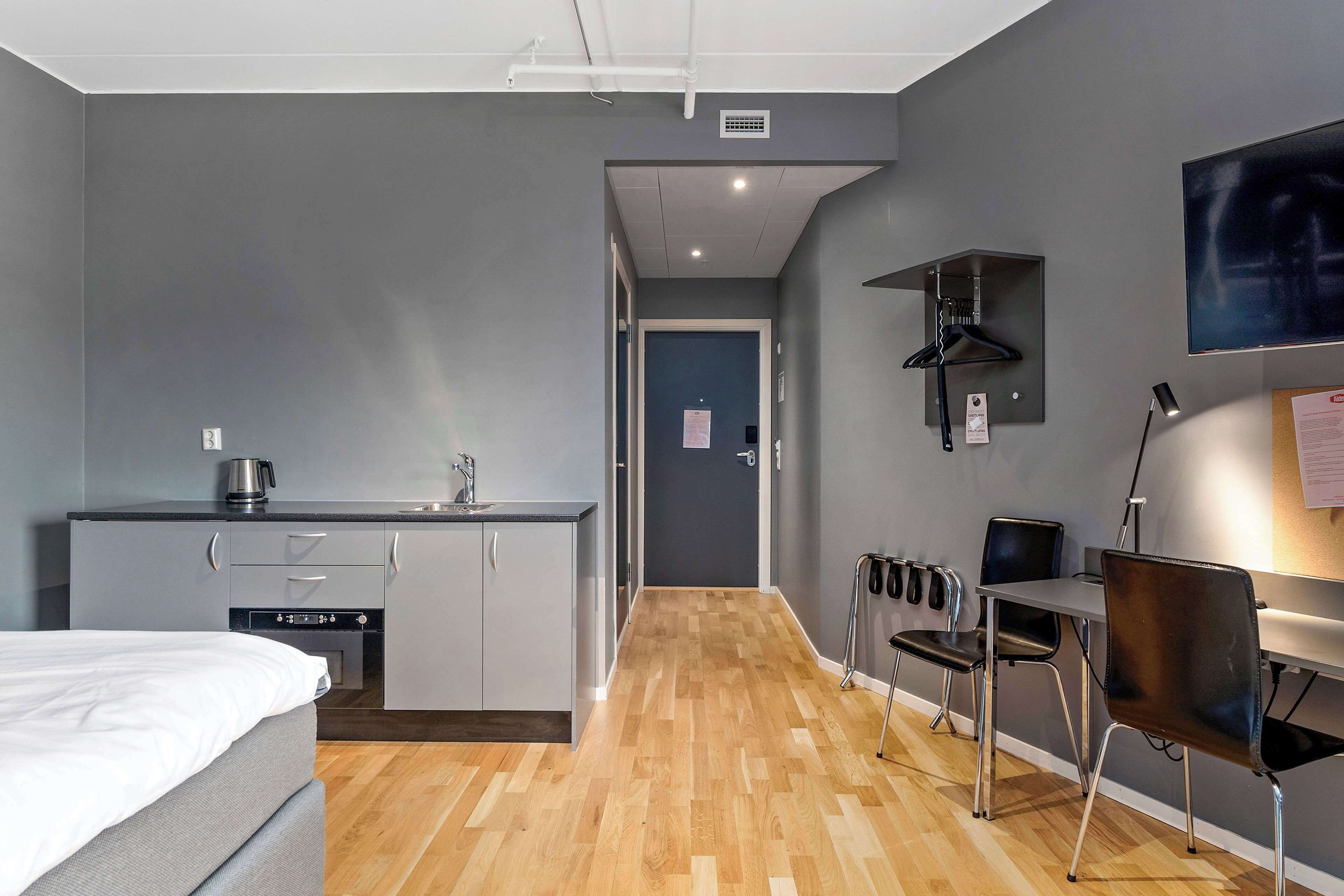 Una habitación de hotel compacta con kitchenette, una cama, un escritorio y una silla.