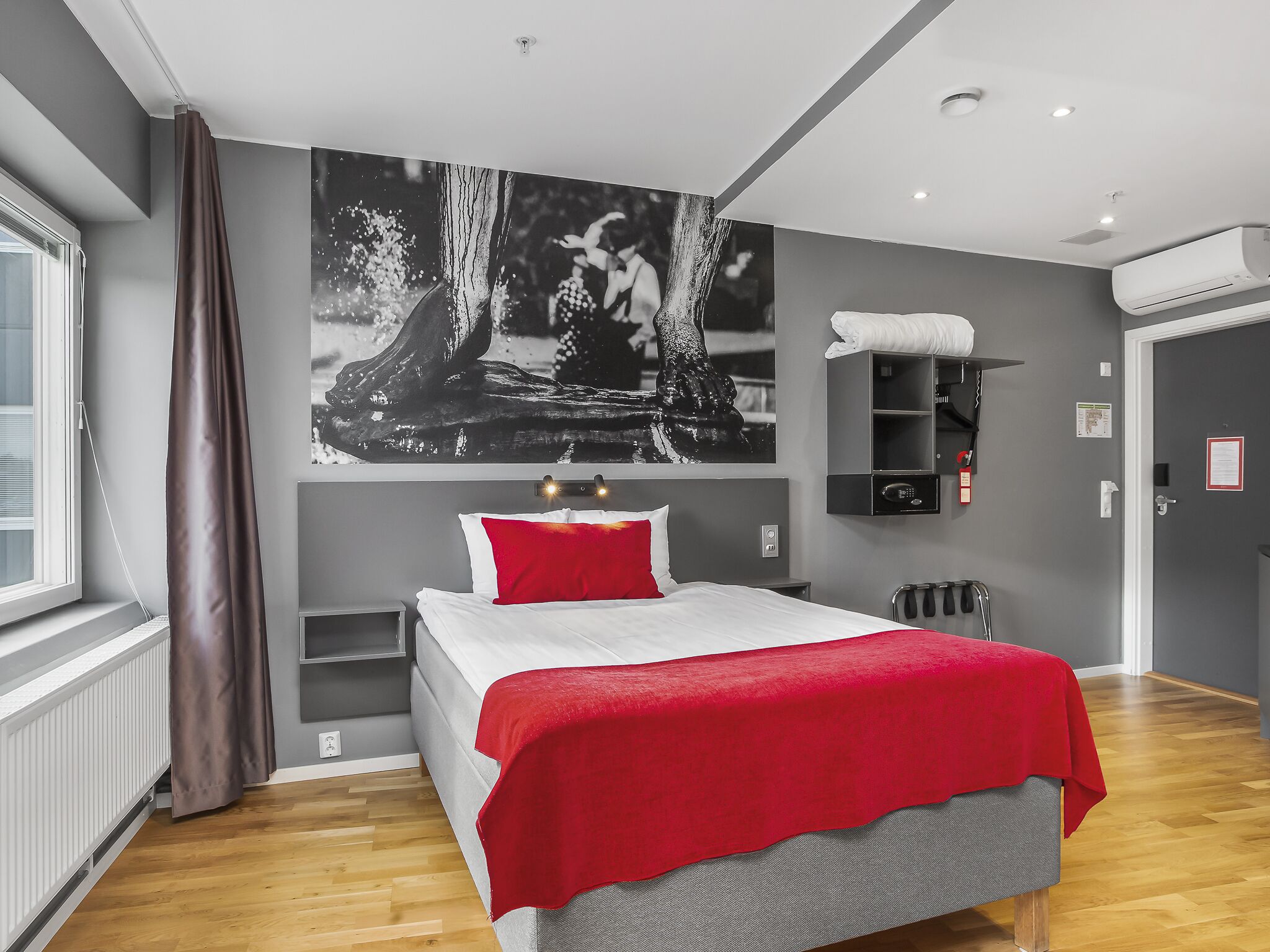 A modern bedroom with a large bed, a red throw, a wall-mounted shelf, and a window with curtains.