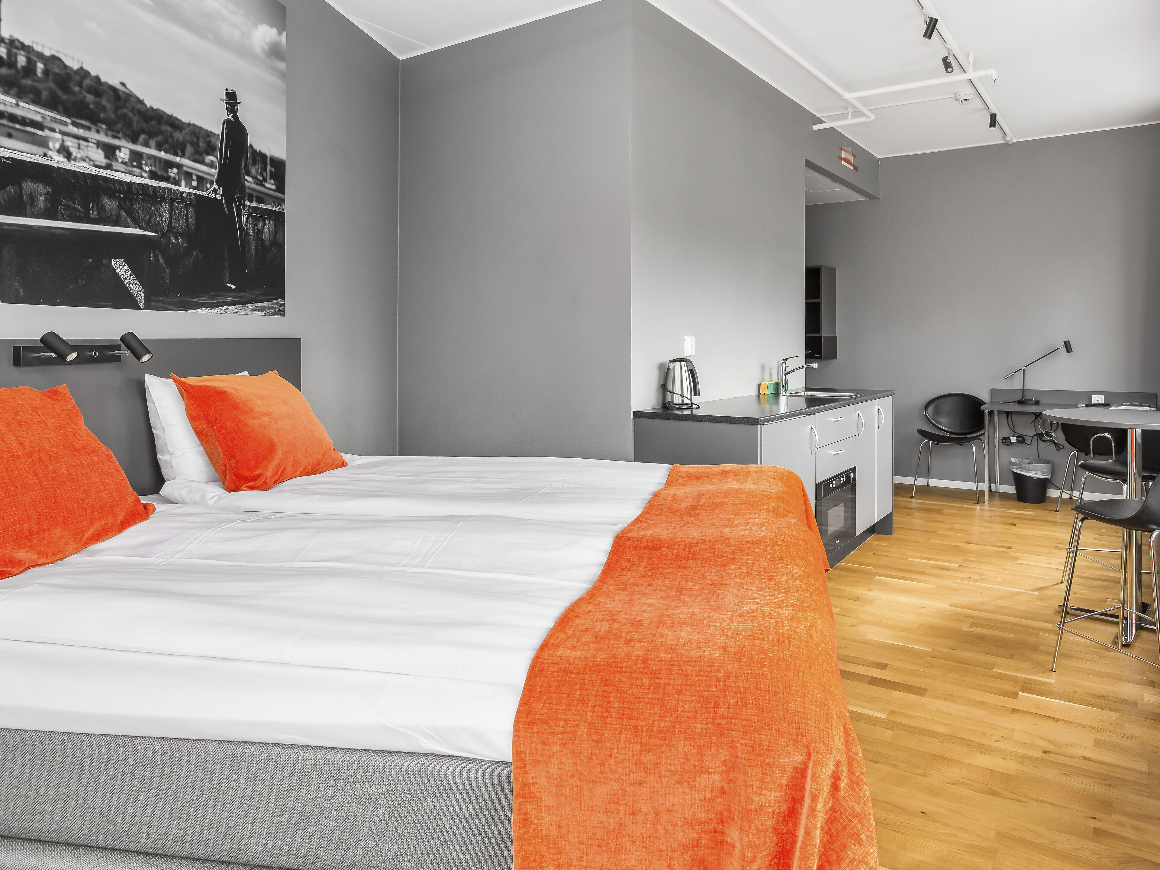 A modern hotel room with a large bed, a desk, and a kitchenette.