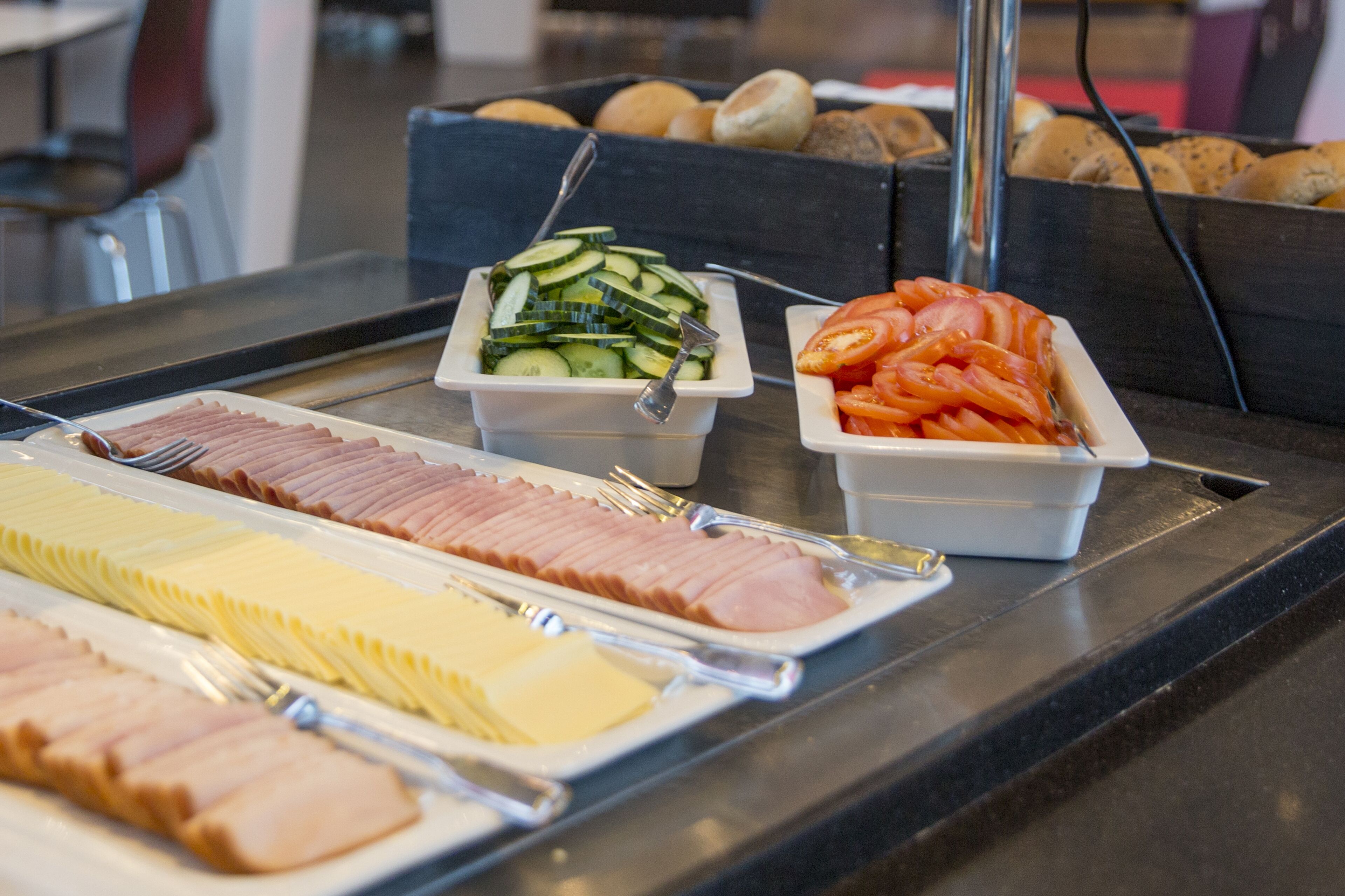 Una mesa de buffet con diversos alimentos, incluyendo jamón en rodajas, queso, pepinos y tomates.